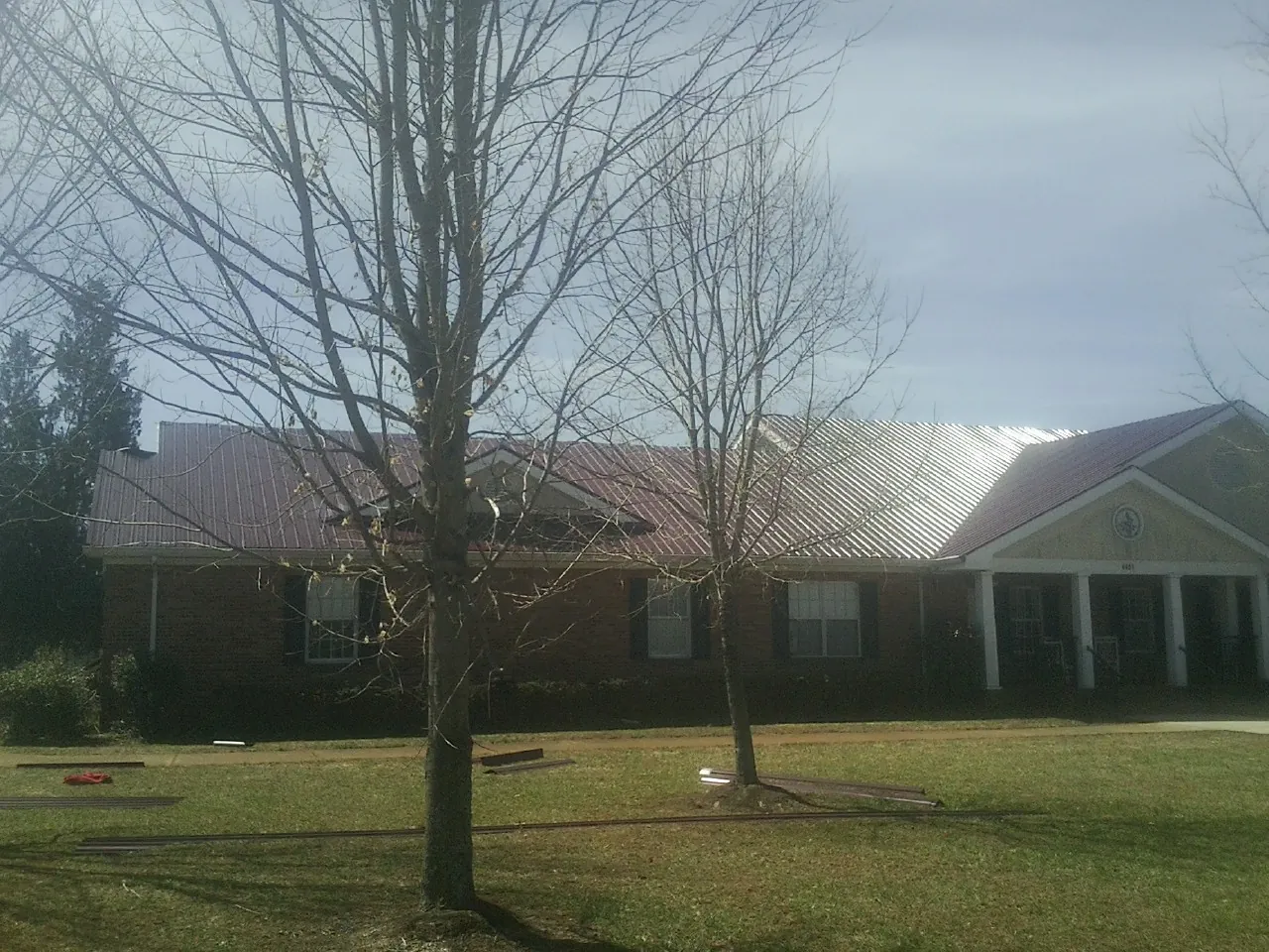 Red metal roof on a brick building seen from the front lawn in Windham