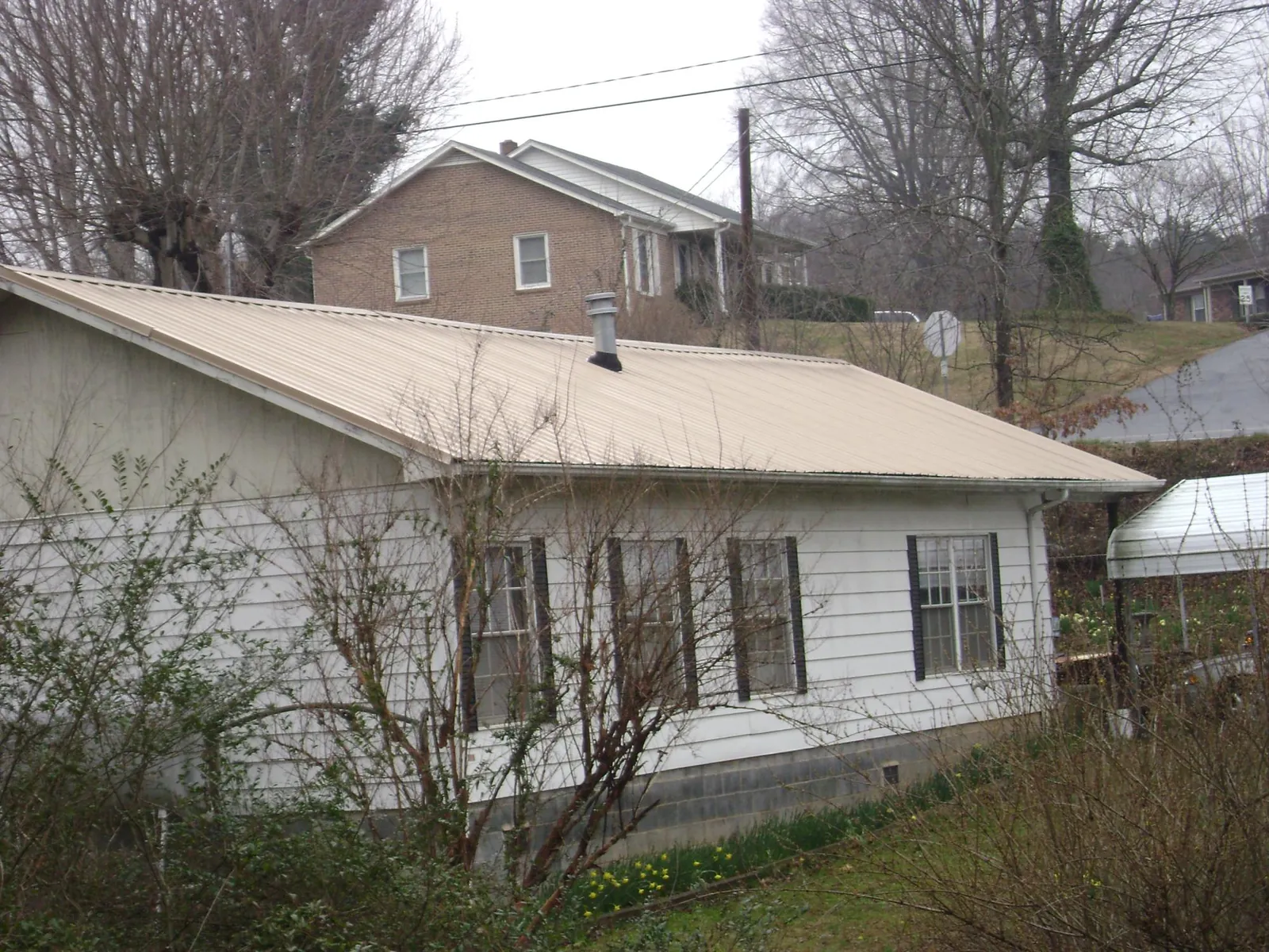 Tan metal roof on a white sided house set into a hillside — Commercial Roofing by Roofing Brothers in Windham